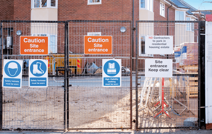 Jobsite safety signs posted at construction site entrance on gate