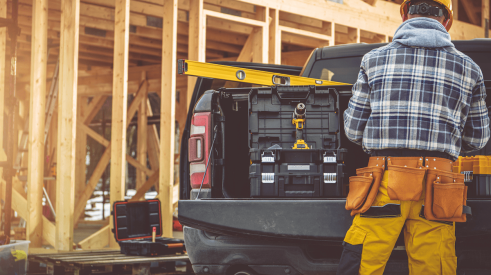 Construction worker standing by work truck with framed house in the background