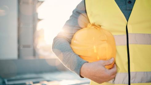Construction worker in yellow vest holding hard hat at hip