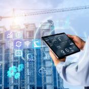 Construction worker at job site looking at tablet, icons floating in front of building that is under construction