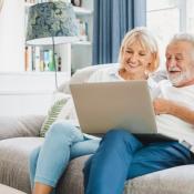 Baby Boomer couple sits on couch looking at laptop together