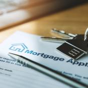 A mortgage application sits on a desk with a pen and a house key on top of it