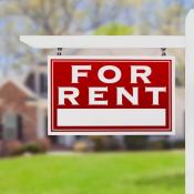 "For Rent" sign posted in a front yard of a single-family home