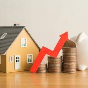 A model home and piggy bank sit next to three stacks of coins placed in ascending order from left to right, indicating financial growth