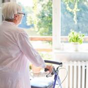 An elderly woman stares out the window of her home