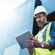 A construction worker uses a software program on a tablet while working on a jobsite