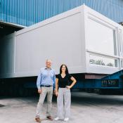 Man and woman by shipping truck with stackable modular apartment pod