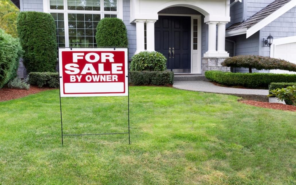 A sign reading "For Sale By Owner" sits in front yard of single-family home