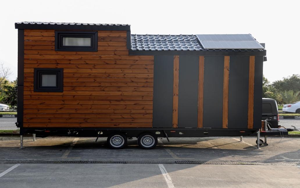 A newly built tiny home sits on trailer in a parking lot ready to be moved to its home