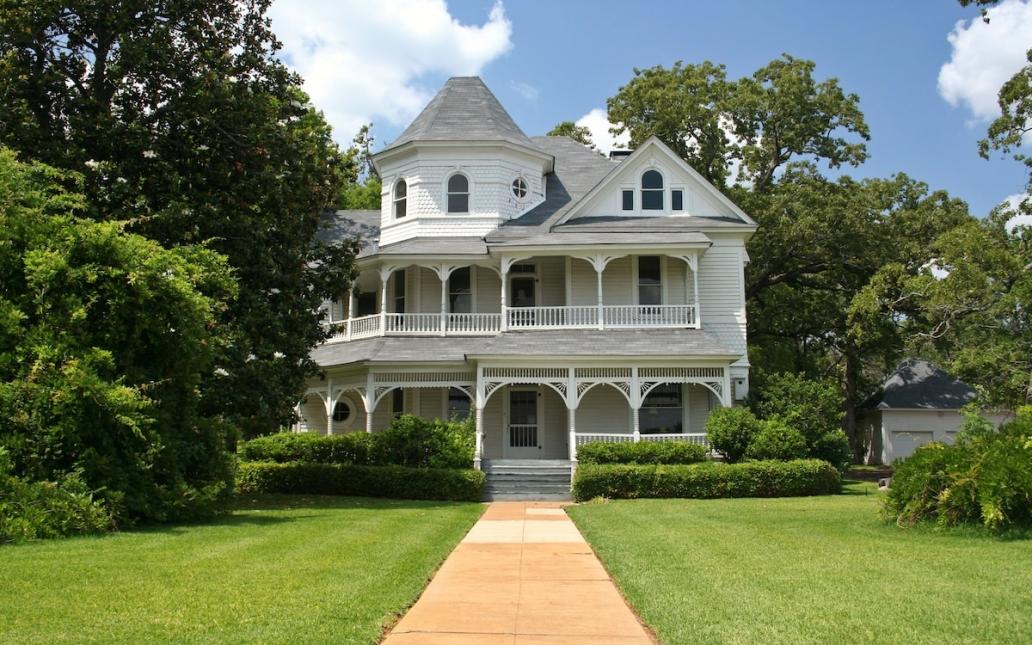 White victorian home sits on large lot lined with trees