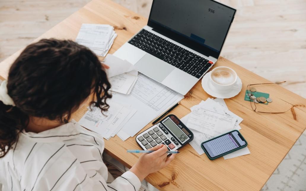 A renter looks over budget with laptop, bills, and calculator at a table