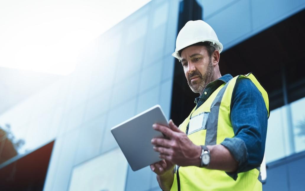 A construction worker uses a software program on a tablet while working on a jobsite