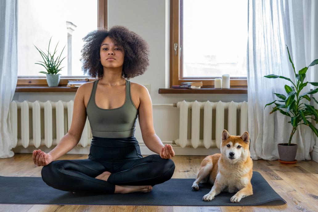Woman doing yoga with dog in home room