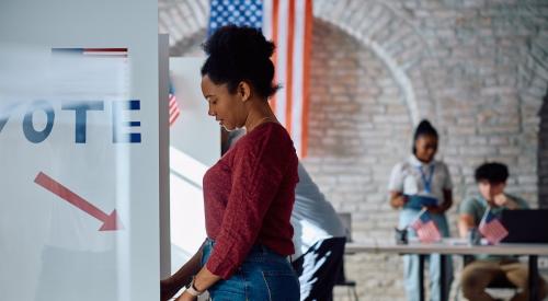 Young woman stands at voting booth filling out ballot