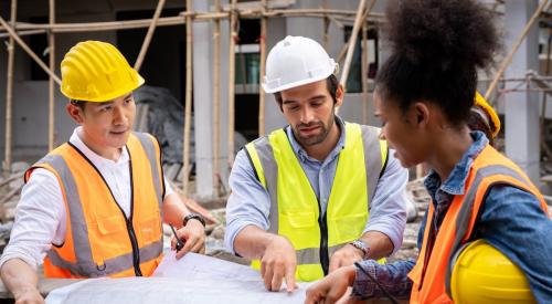Three construction workers discuss plans at a jobsite