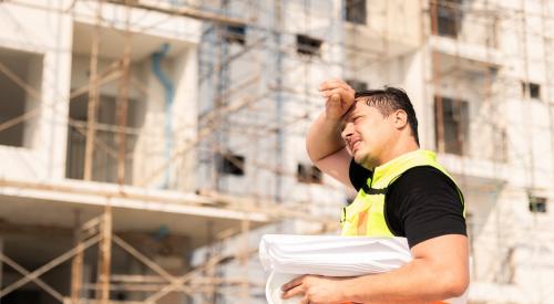 A construction worker stands in the sun wiping sweat from forehead