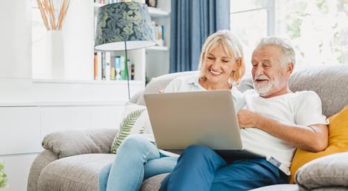 Baby Boomer couple sits on couch looking at laptop together