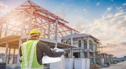 Construction worker looking over plans and staring at framed house in background