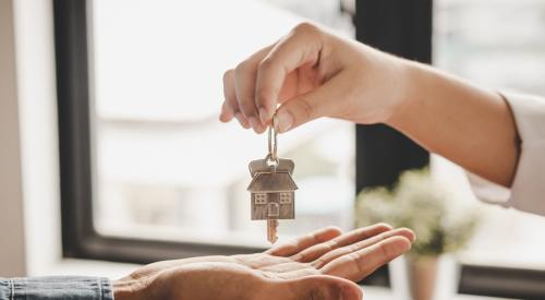 One person hands over key with small house keychain attached to another individual 