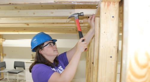 Carpentry student nails hammer into wall 