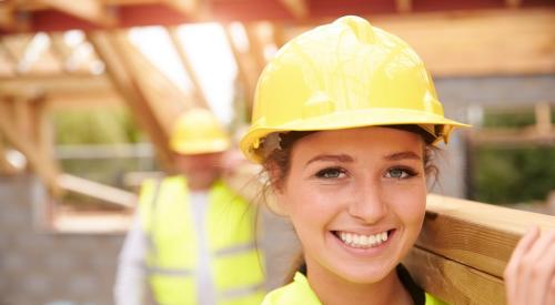 Female construction worker carries lumber through jobsite