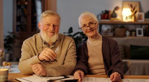 A Baby Boomer couple sits at a table, going over home bills.