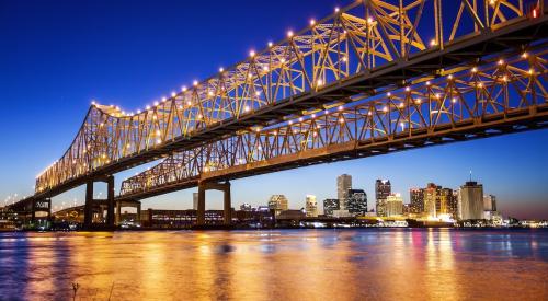 A bridge in New Orleans is illuminated at night with the city skyline behind it