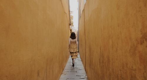 Woman walking in narrow space between two tall walls