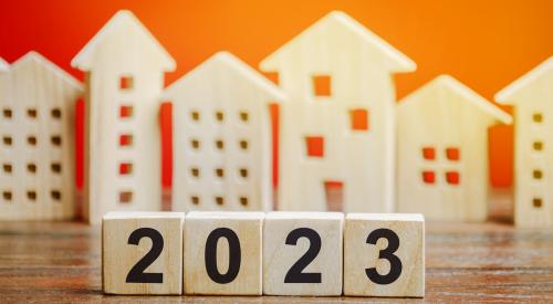 Numbered wooden blocks that say '2023' in front of wooden house models with orange background