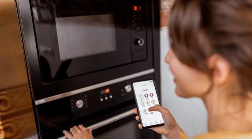Woman holding smart phone and using smart oven appliance