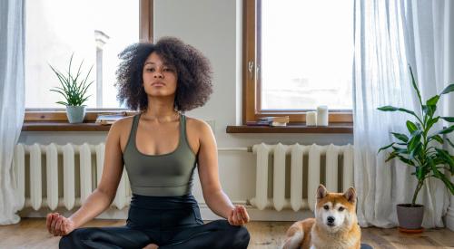 Woman doing yoga with dog in home room