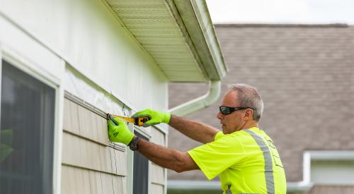 Construction worker measuring exterior trim of house