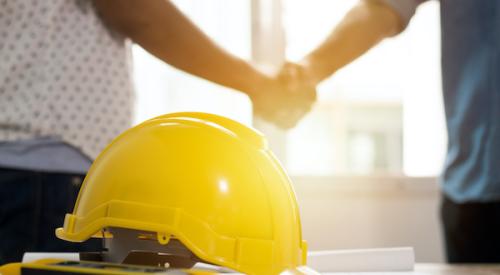 Two people shaking hands with hard hat in foreground