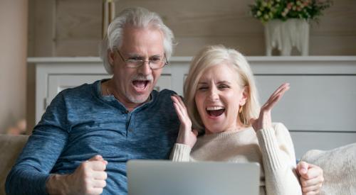 Older couple smiling, cheering to laptop