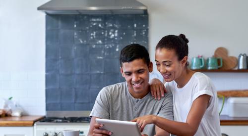 Couple in kitchen smiling together while looking at tablet