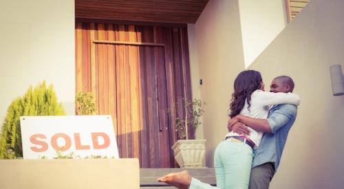 Happy couple hugging next to sold home sign