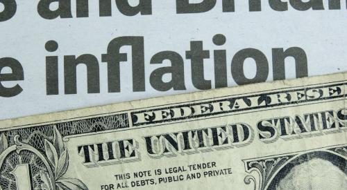 Dollar bill with Federal Reserve stamp on top of newspaper with inflation headline