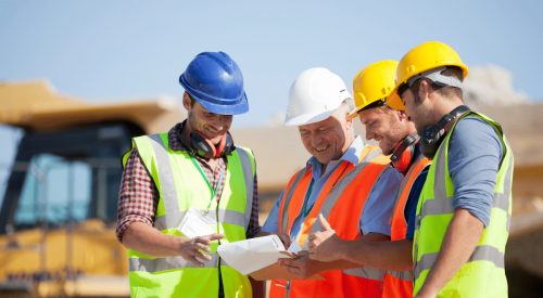 Group of smiling home builders wearing hard hats on a construction site