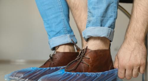 Man slipping footies over brown shoes.