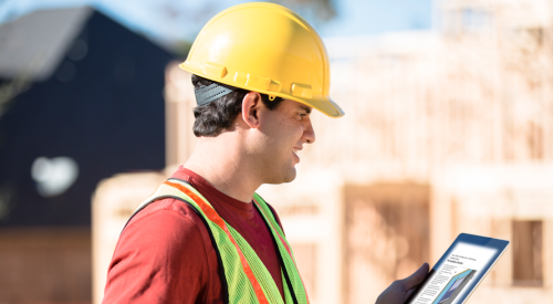 Construction worker wearing hard hat and looking at tablet with specifications on building jobsite