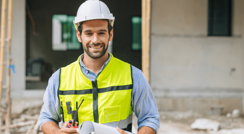 Smiling home builder holding a rolled set of house plans under his arm