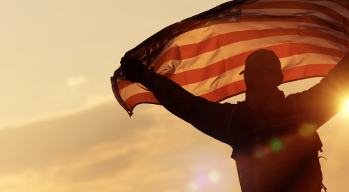Veteran with unfurled United States flag at sunset