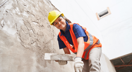 Woman construction worker applying stucco to wall on jobsite