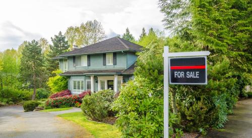 Black and red for-sale sign outside of green home