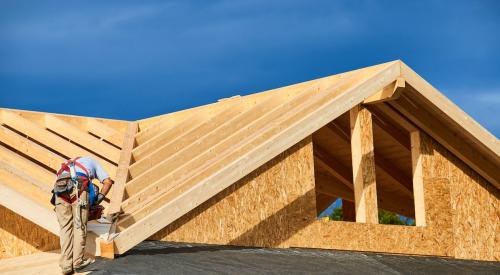 Home builder on roof of new wood-framed house