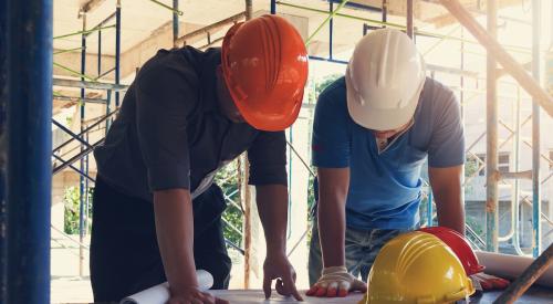 Builders with hard hats looking at house plans on table 