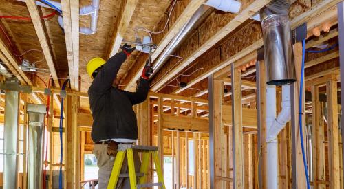 Home builder standing on ladder installing downlight in wood-framed ceiling 