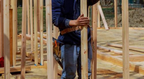 Carpenter holds wood framing member in house under construction