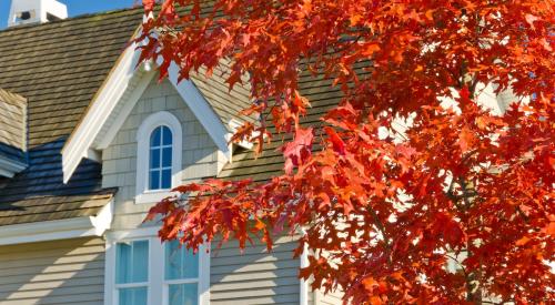 Upper level of residential house behind tree with red fall leaves