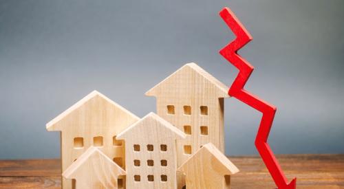 Small wooden apartment models next to falling red arrow on wooden table